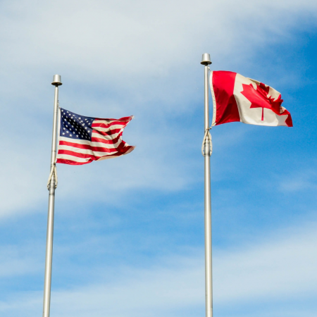 Picture of the American and Canadian flags on a pole against the sky.